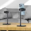Two black phone stands are displayed on a wooden table in front of a blurred gray sofa. Produktbild-Vorschau