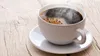 A white cup of steaming coffee sits on a wooden table. Voir les images du produit
