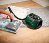 A person is using a vacuum pump to compress items in a storage bag, with the pump unit visible. Produktbild-Vorschau