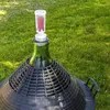 A fermentation airlock and stopper are attached to a large green glass carboy, which is sitting on a lawn. Produktbild-Vorschau