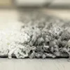 A close-up view of a shaggy rug with a checkered pattern in white and gray. Náhľad obrázku produktu