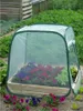 A pop-up greenhouse with flowers inside, placed in a garden. Produktbild-Vorschau