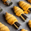 Several baked pastry cones are arranged on a baking sheet, each on a metal mold. Podgląd zdjęcia produktu