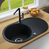 A black granite kitchen sink with a silver faucet is shown on a wooden countertop, with a window and fruit in the background. Produktbild-Vorschau
