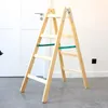 A wooden stepladder is shown in a room with a white door and a white wall. Produktbild-Vorschau
