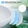 A close-up view of a white oval basin with layers of blue and white material underneath, suggesting a multi-layered glaze. The background features green leaves with water droplets, and a circular inset shows water droplets on a white surface. Anteprima dell’immagine prodotto