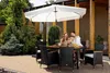 A couple enjoys a meal outdoors under a large white umbrella, seated at a polyrattan dining set with an acacia wood table. Náhľad obrázku produktu