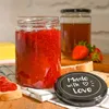 A jar of strawberry jam and a jar of honey are displayed on a wooden surface with bread and strawberries. Produktbild-Vorschau