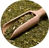 A wooden scoop filled with dried green mate tea leaves and other herbs. Produktbild-Vorschau