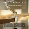 A monitor arm clamped to a wooden desk, with text overlays explaining setup options and desk thickness. Produktbild-Vorschau