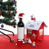 A Christmas-themed scene with a decorated tree, a bottle of wine with a Santa hat, and a small red house decoration. Náhled obrázku produktu