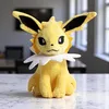 A yellow plush toy of a Pokemon character sitting on a marble-patterned surface, with a blurred office-like background. Produktbild-Vorschau