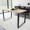 A modern dining table with a light wood top and black metal legs, placed on a textured rug in a well-lit room. Decorative items are on the table. Produktbild-Vorschau