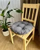 A round gray cushion sits on a wooden chair next to a potted plant. Produktbild-Vorschau