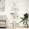 A white bookshelf filled with books and decorative items, placed in a living room next to a sofa and a large plant. Náhled obrázku produktu