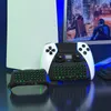 Gaming accessories, including a controller with a keyboard attachment, are displayed on a reflective surface in front of a gaming console and monitor. Produktbild-Vorschau