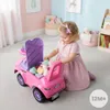 A young child is playing with a pink ride-on toy car filled with stuffed animals and blocks in a brightly colored room. Produktbild-Vorschau