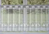 A white lace curtain with a deer and snowflake pattern hanging in a window. Produktbild-Vorschau