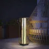 A rattan floor lamp with a twisted design is placed on a patio next to a hanging chair. Podgląd zdjęcia produktu