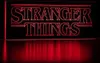 The Stranger Things logo illuminated in red against a black background, with a red reflection on a surface below. Produktbild-Vorschau