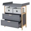 A gray changing table with wooden accents and two fabric storage boxes with stars on top. Produktbild-Vorschau