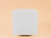 A white cube-shaped product with rounded edges is centered on a light peach background. Produktbild-Vorschau