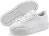 A pair of white Puma Karmen L women's sneakers are shown from a slightly elevated angle, with one shoe in the foreground and the sole of the other shoe visible behind it. Produktbild-Vorschau