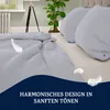 A bed with light gray bedding and pillows, with decorative feathers floating around. Produktbild-Vorschau