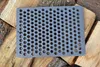 A gray cast iron grate with many circular holes rests on a pile of chopped wood. Produktbild-Vorschau