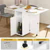 A white folding dining table with storage compartments and chairs in a room. Produktbild-Vorschau