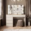 A vanity table with a mirror and lights, a stool, and decorative items in a room. Produktbild-Vorschau