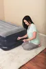 A woman is kneeling next to an inflatable mattress, adjusting the pump valve. Náhled obrázku produktu