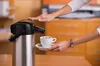 A person pouring coffee from a large airpot into a cup. Produktbild-Vorschau