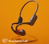 A pair of black and red bone conduction headphones are shown floating against an orange background. Náhled obrázku produktu