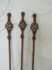 Three rusty metal garden stakes with twisted decorative tops stand against a textured white wall. Produktbild-Vorschau