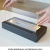 A person's hands are shown placing a glass shield onto a black tabletop fireplace. Náhľad obrázku produktu