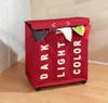 A red laundry sorter with three compartments labeled 'DARK', 'LIGHT', and 'COLOR' stands on a wooden floor next to a white slatted door. Náhľad obrázku produktu