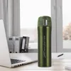 A green insulated travel mug sits on a desk next to a laptop, with office supplies in the background. Anteprima dell’immagine prodotto
