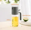 A glass oil sprayer with a gray lid and handle, filled with yellow oil, is shown on a table with a blurred background of greenery and a sliced lime in the foreground. Produktbild-Vorschau
