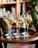 Six wine glasses filled with white wine are arranged on a tray, with a bottle of wine in the background. Produktbild-Vorschau
