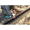 A person is kneeling on a garden pad and using a hammer to install a black plastic edging strip into the ground. Produktbild-Vorschau