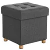 A dark gray upholstered storage ottoman with wooden legs is shown against a white background. Náhled obrázku produktu