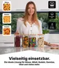 Vier klare Glasvorratsgläser mit Bambusdeckeln auf einer Küchenarbeitsplatte, gefüllt mit Bohnen, Pasta, Bonbons und Müsli, mit einer Frau dahinter Produktbild-Vorschau