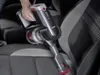 A hand holding a cordless vacuum cleaner while cleaning car seats. Produktbild-Vorschau