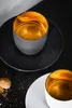 Two espresso cups with gold interiors sit on black and white saucers on a dark surface, with a cookie and crumbs nearby. Náhled obrázku produktu