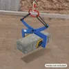 A blue stone lifting clamp is holding a gray concrete block, suspended by a red and silver carabiner. The background is a sandy, construction-like environment. Náhled obrázku produktu