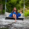 A woman sits on a swing over a river, wearing a blue dress. Podgląd zdjęcia produktu