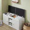 A white storage bench with its lid open, revealing organized items inside, placed against a light green wall. Produktbild-Vorschau