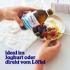 A person is pouring omega-3 oil from a bottle into a bowl of yogurt with berries and granola. Produktbild-Vorschau