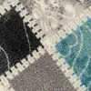 A close-up view of a patterned rug with geometric shapes in gray, black, white, and turquoise. Produktbild-Vorschau